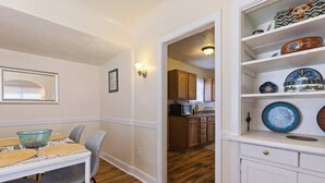 A dining area with a table set for four, a kitchen in the background, and a shelf with decorative plates. - Hot Summer Deals Cute Clean Quiet Dog Friendly (Phoenix)