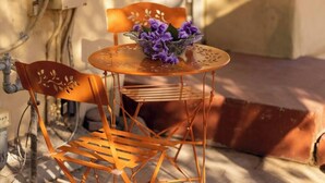 A small outdoor seating area with a metal table and chairs, a metal chair with a decorative backrest, and a metal basket with purple flowers. - Hot Summer Deals Cute Clean Quiet Dog Friendly (Phoenix)