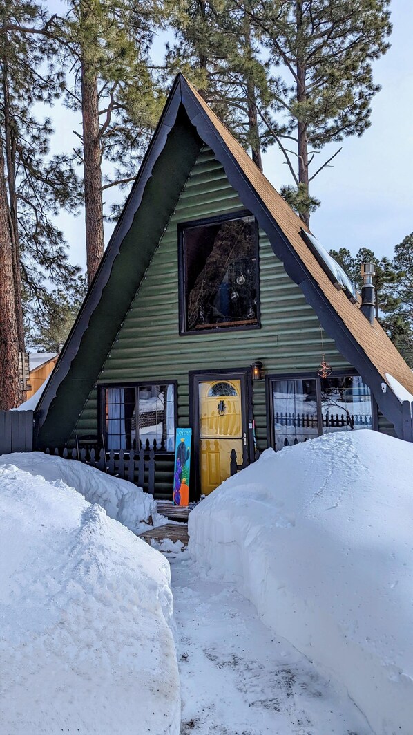 A cabin with a triangular roof, a large window, and a wooden door.