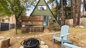 Een driehoekige hut met een houten terras, een vuurkorf en een blauwe Adirondack-stoel.