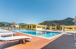A swimming pool with sun loungers and a view of a hillside. - Hotel Fiore di Maggio (Villasimius)