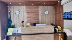 A reception desk with two clocks, a television, and a plant.