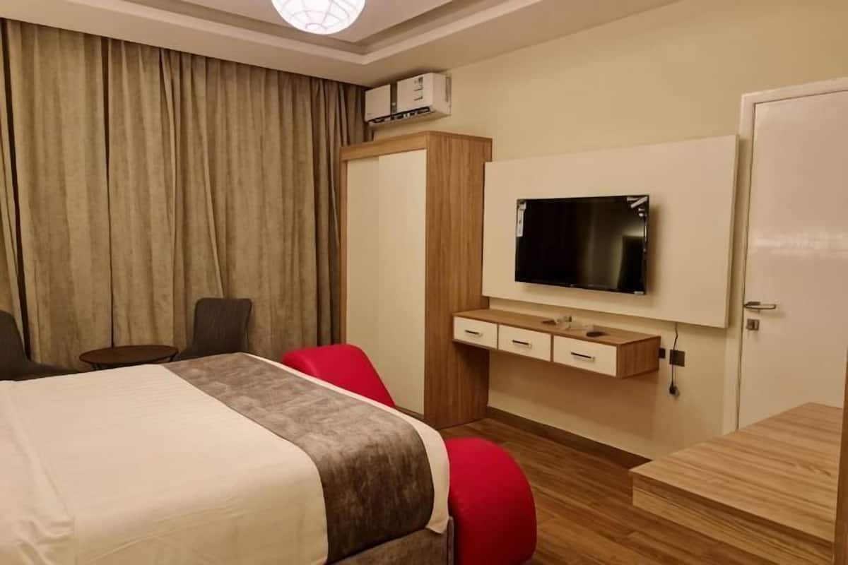 A hotel room with a bed, a TV mounted on the wall, a desk, and a wardrobe.