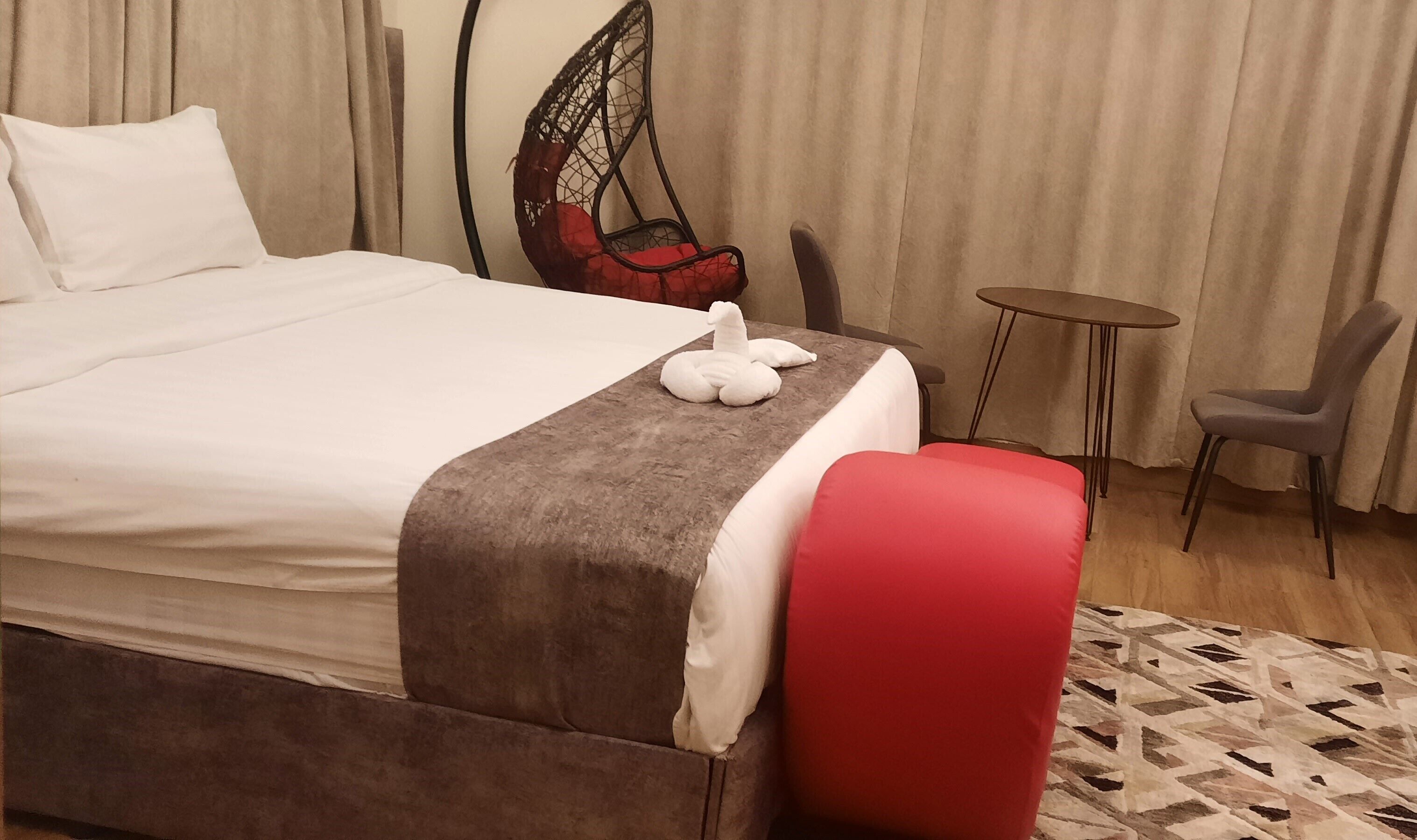 A hotel room with a bed, a red chair, a small round table, and a decorative wall hanging.