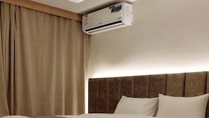 A hotel room with a bed, a headboard, an air conditioning unit, and a wooden floor.