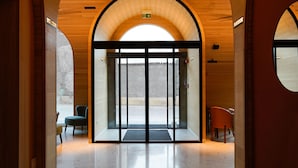 Un pasillo con arcos de techo de madera, una entrada con puerta de cristal y un banco.