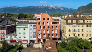 Un edificio de varios pisos con una fachada roja característica, rodeado de otros edificios y vegetación.