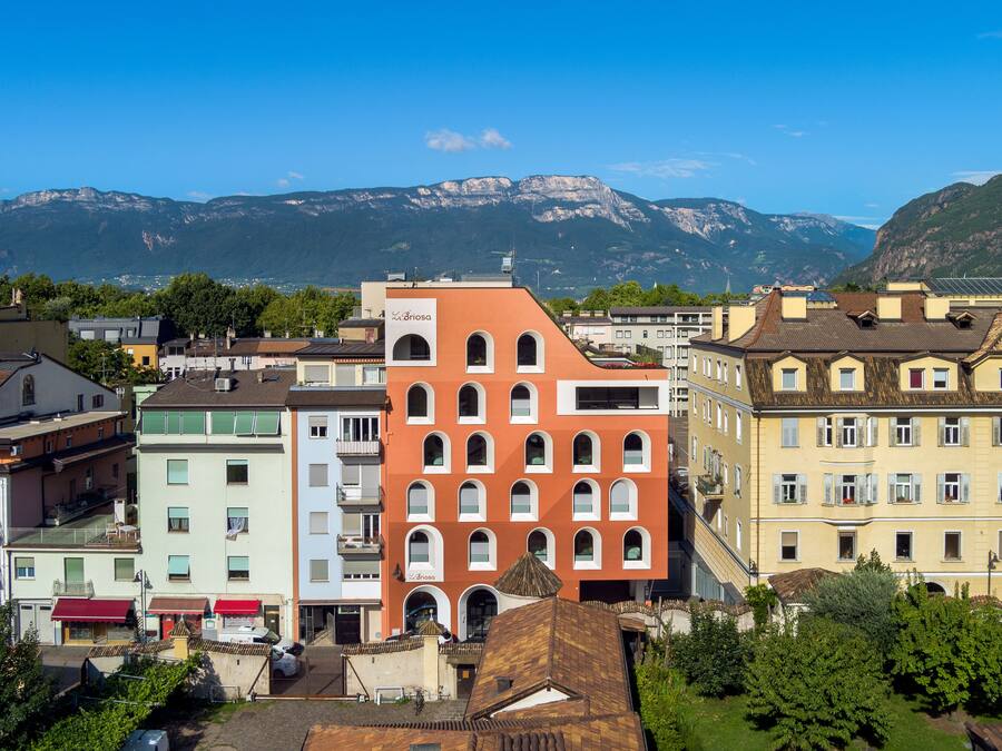 Um edifício de vários andares com uma fachada vermelha marcante, rodeado por outros edifícios e vegetação.