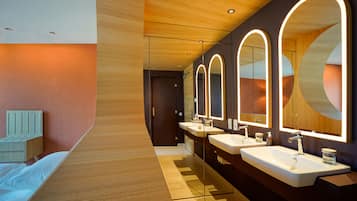 A modern bathroom with a wooden floor, a bed, and a long vanity with three sinks and mirrors.