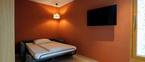 A bedroom with a bed, a wall-mounted TV, and a window.