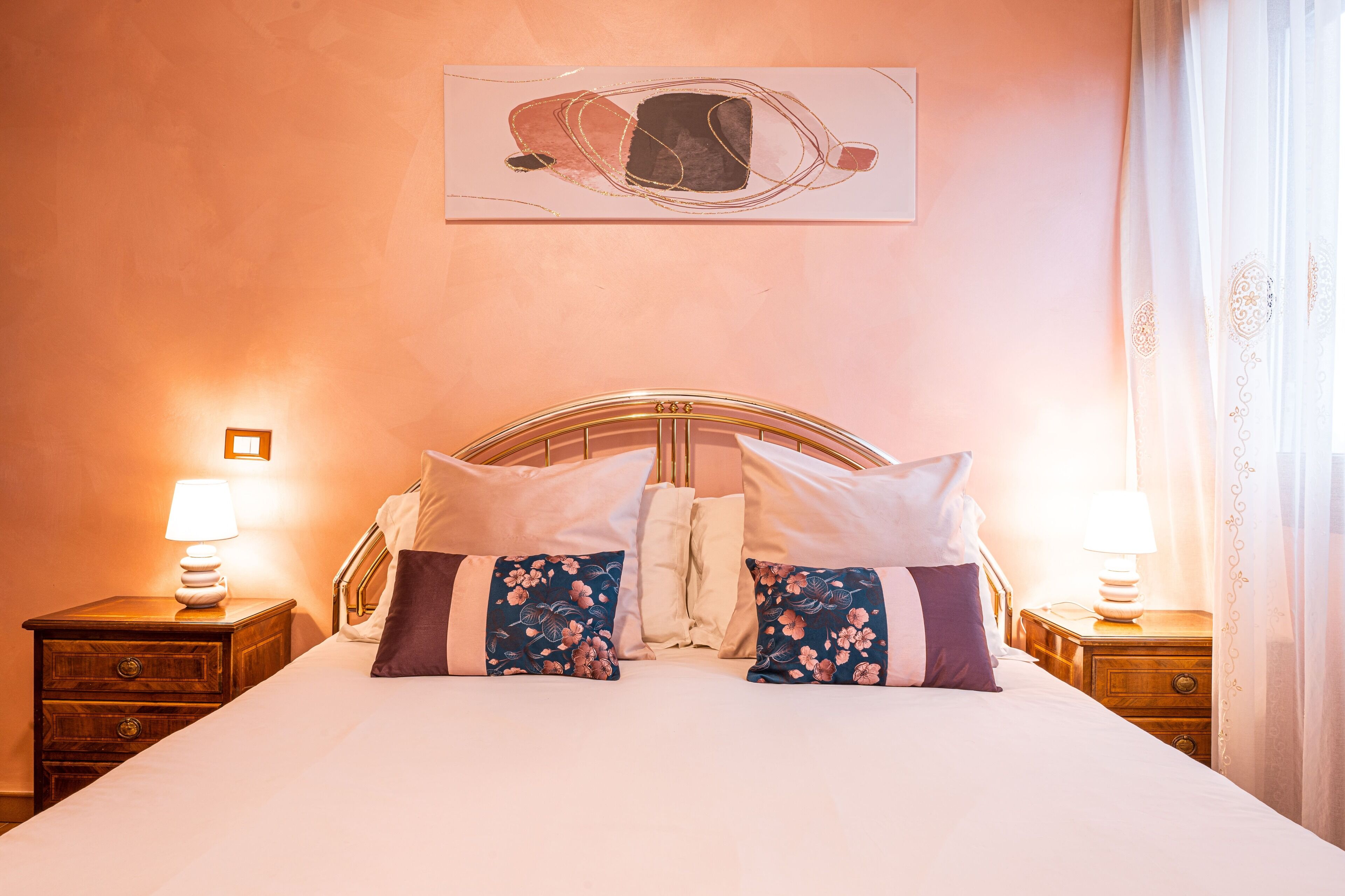 A neatly made bed with floral pillows, a wooden headboard, and a wall-mounted artwork.