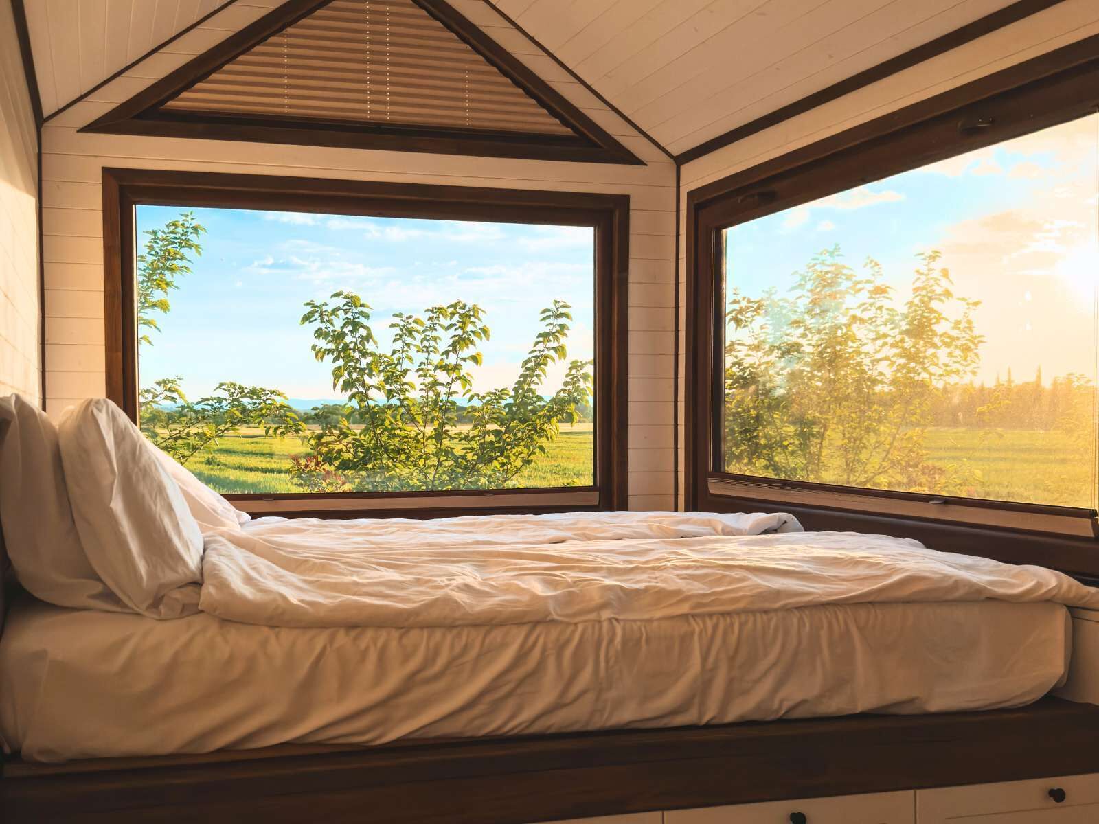Een slaapkamer met een bed, grote ramen en uitzicht op een groen landschap.