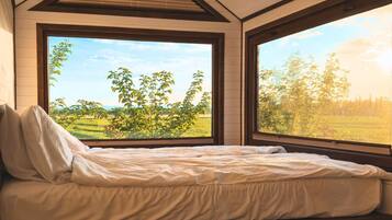 Een slaapkamer met een bed, grote ramen en uitzicht op een groen landschap.