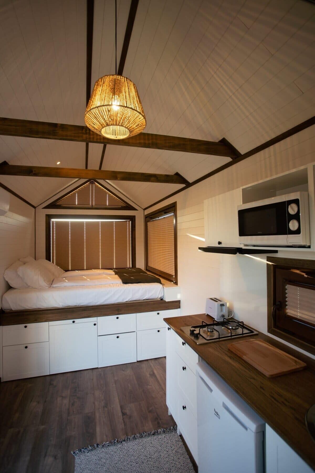 A compact bedroom with a bed, bedside tables, and a hanging light fixture.