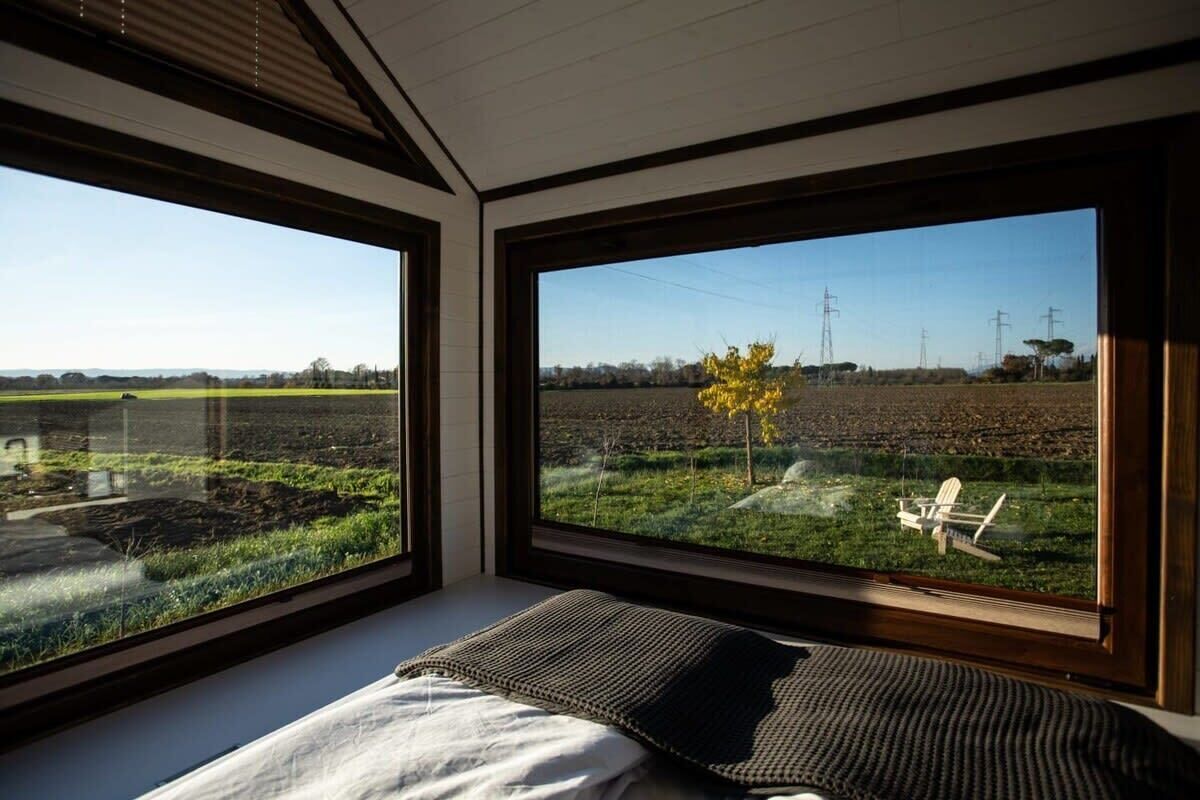 Een slaapkamer met grote ramen en uitzicht op een veld en windturbines.