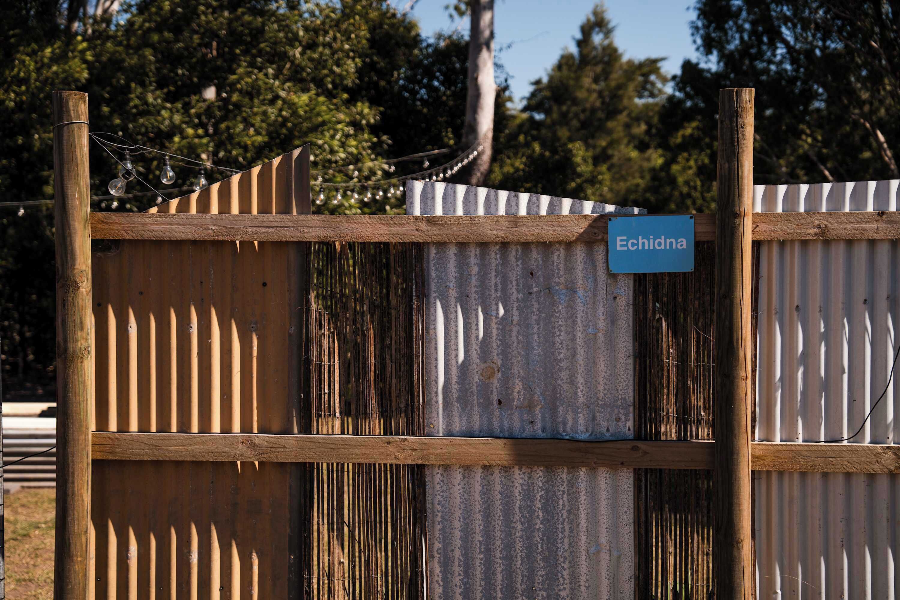 A corrugated metal fence with a wooden post and a sign that reads 'Echidna'.