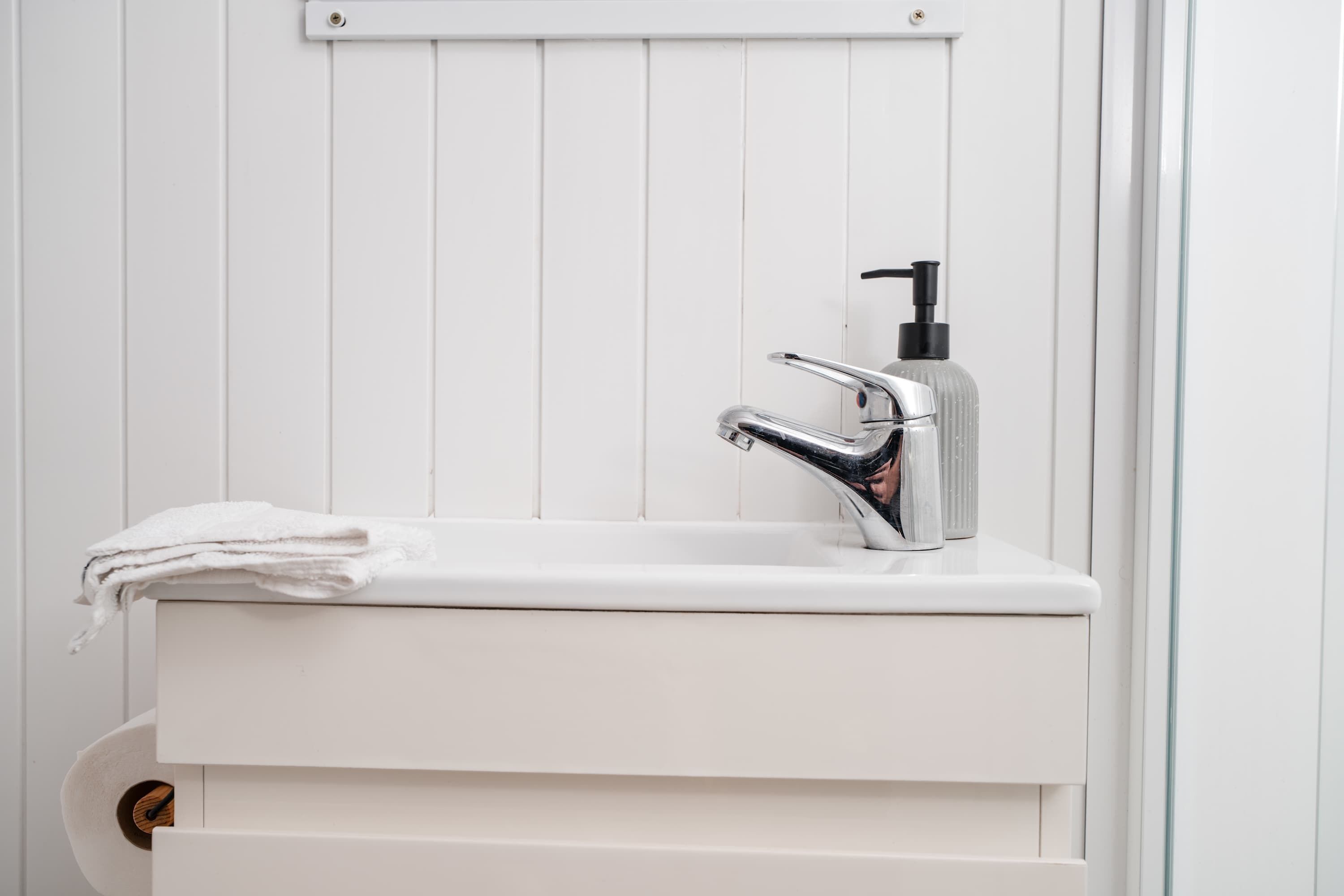 Ein weißes Waschbecken mit einem modernen Wasserhahn und einer Seifenspender.