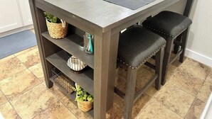 Une table à manger avec quatre sets de table gris foncé, deux chaises noires rembourrées et des étagères avec des paniers et des objets décoratifs.