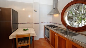 Une cuisine de taille réduite équipée d’un réfrigérateur, d’une cuisinière, d’un évier et d’une fenêtre agrémentée d’une grille décorative.