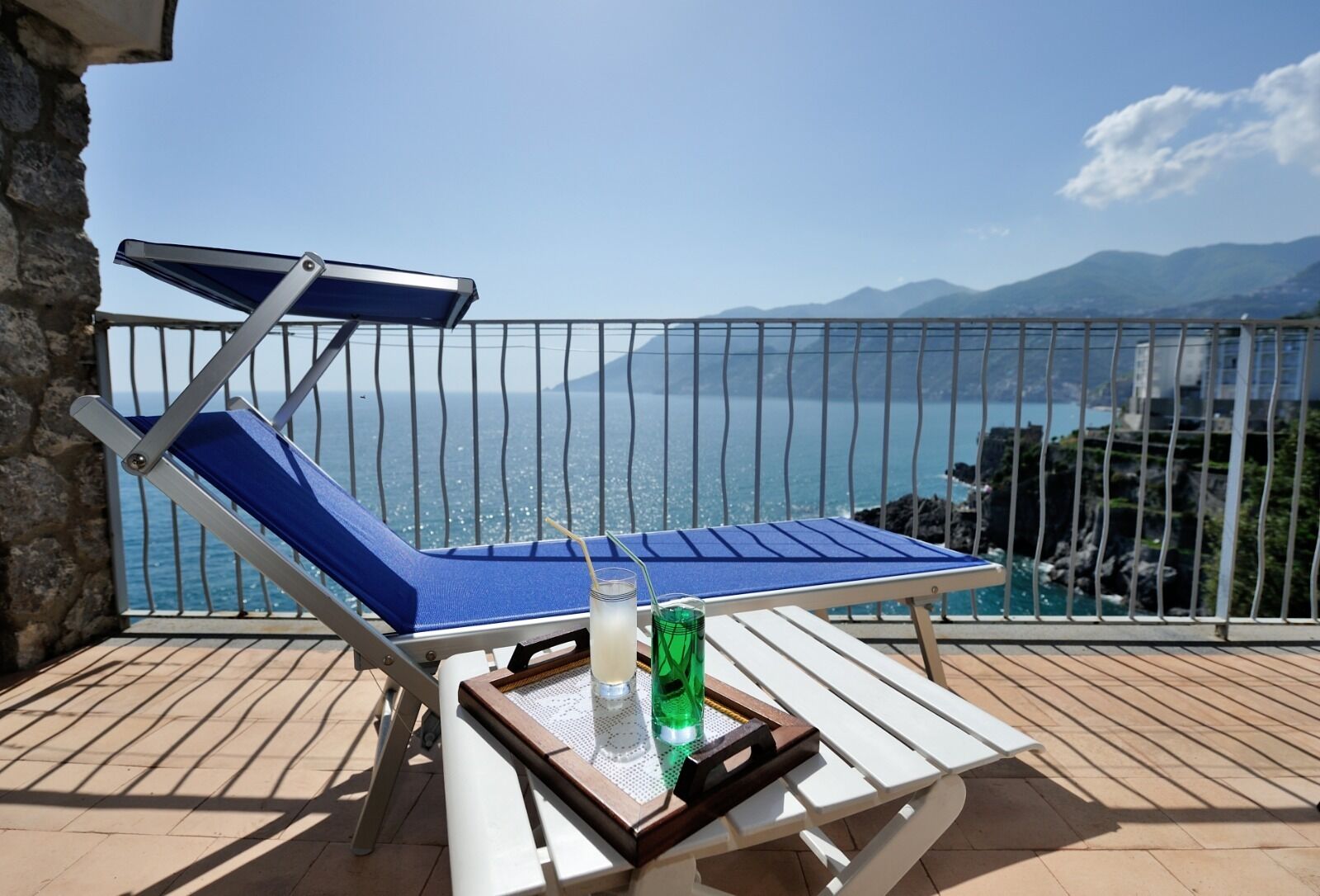 Una tumbona con una mesa y bebidas en un balcón con vistas al mar.