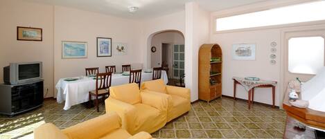 A living room with yellow sofas, a dining area with a table set for four, a television, and a bookshelf.