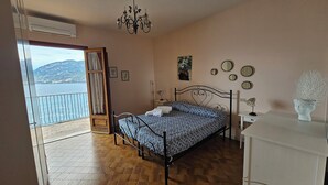 Une chambre à coucher avec un lit, une table de chevet, une lampe, un miroir et une vue sur la mer.