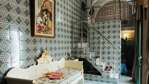 Une pièce avec un papier peint à motifs, un canapé blanc, une petite table ronde et un escalier doté d’une rampe en métal.
