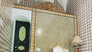 Une pièce dont les murs sont recouverts de carreaux à motifs, avec une chaise en bois, une table sur laquelle se trouve une lampe et un tapis.