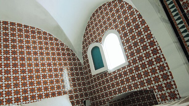 Une pièce avec un lit, une fenêtre et des murs décorés de motifs.