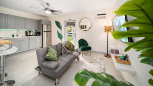 A modern kitchen with grey cabinets, a grey sofa with green cushions, a green armchair, and a floor lamp.