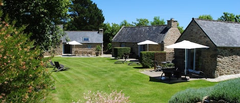 A stone house with a well-maintained lawn, outdoor seating, and a clear blue sky.