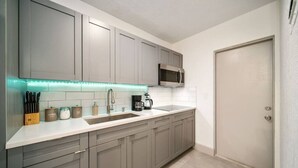 Una cocina moderna con armarios grises, un lavamanos de acero inoxidable y un microondas.