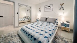 Un dormitorio con cama, mesitas de noche, ventilador de techo, espejo y televisor montado en la pared.