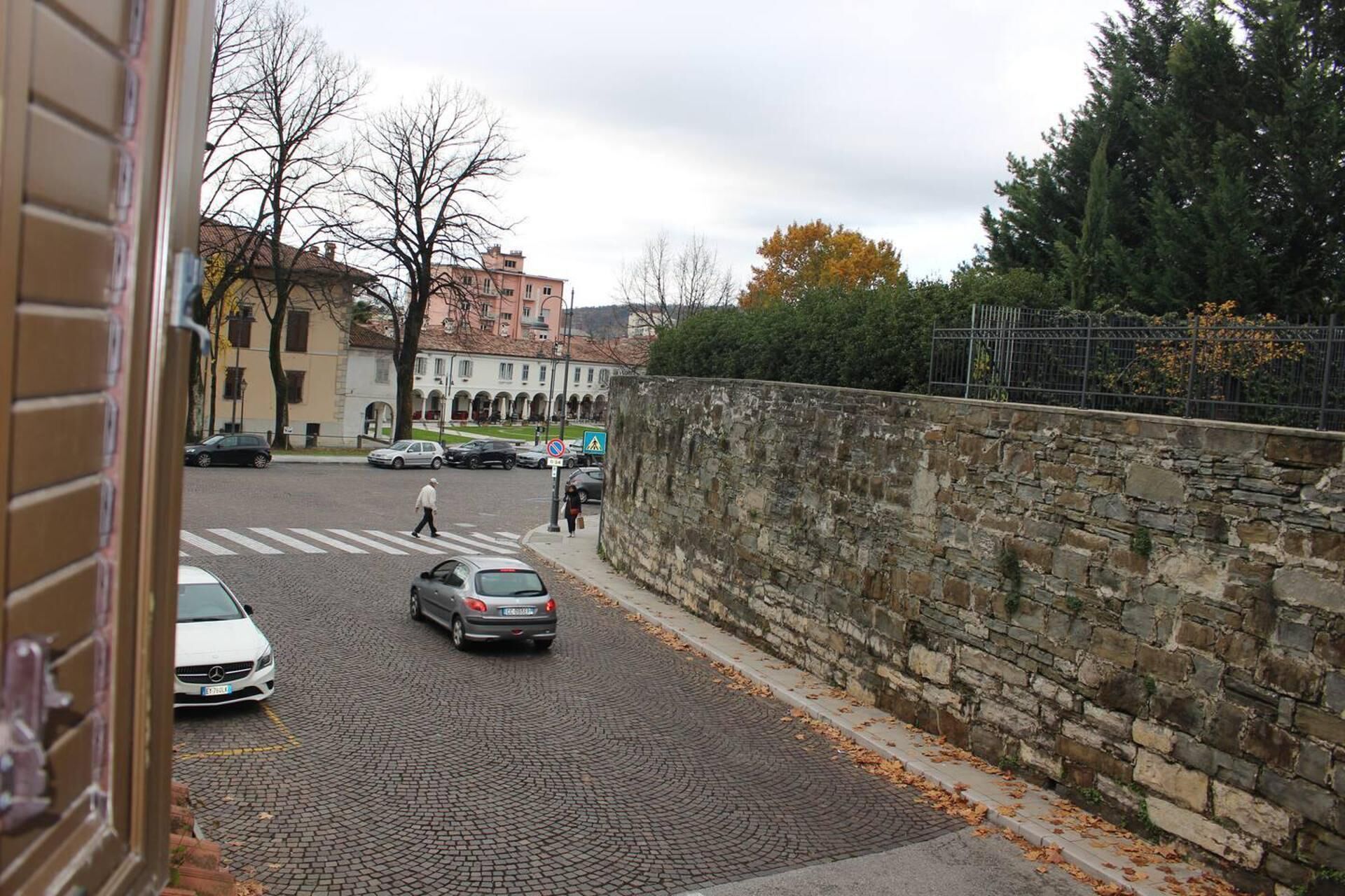 A cobblestone street with parked cars and a pedestrian crossing.