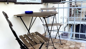 Un balcon avec une table et des chaises, un bol bleu et une vue sur l’intérieur du bâtiment.