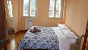 Une chambre à coucher avec un lit, deux fenêtres, un radiateur et un plancher en bois.
