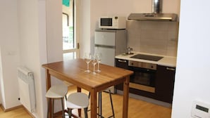 Une cuisine compacte avec une table en bois, deux tabourets blancs, un four à micro-ondes, un réfrigérateur et une hotte aspirante en acier inoxydable.