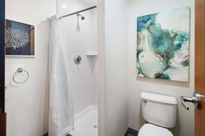 A bathroom with a shower, toilet, and abstract art on the wall.