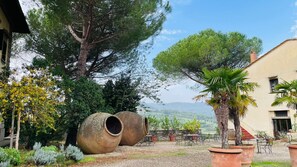 A courtyard with large terracotta pots, a palm tree, and a building with a red roof. - Corte di Valle Wine and Resort (Greve in Chianti)