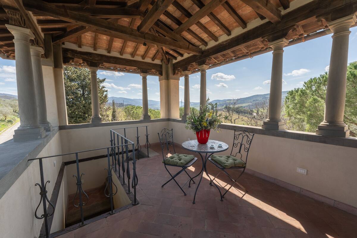 Un patio techado con mesa y sillas, con vistas a un paisaje pintoresco.
