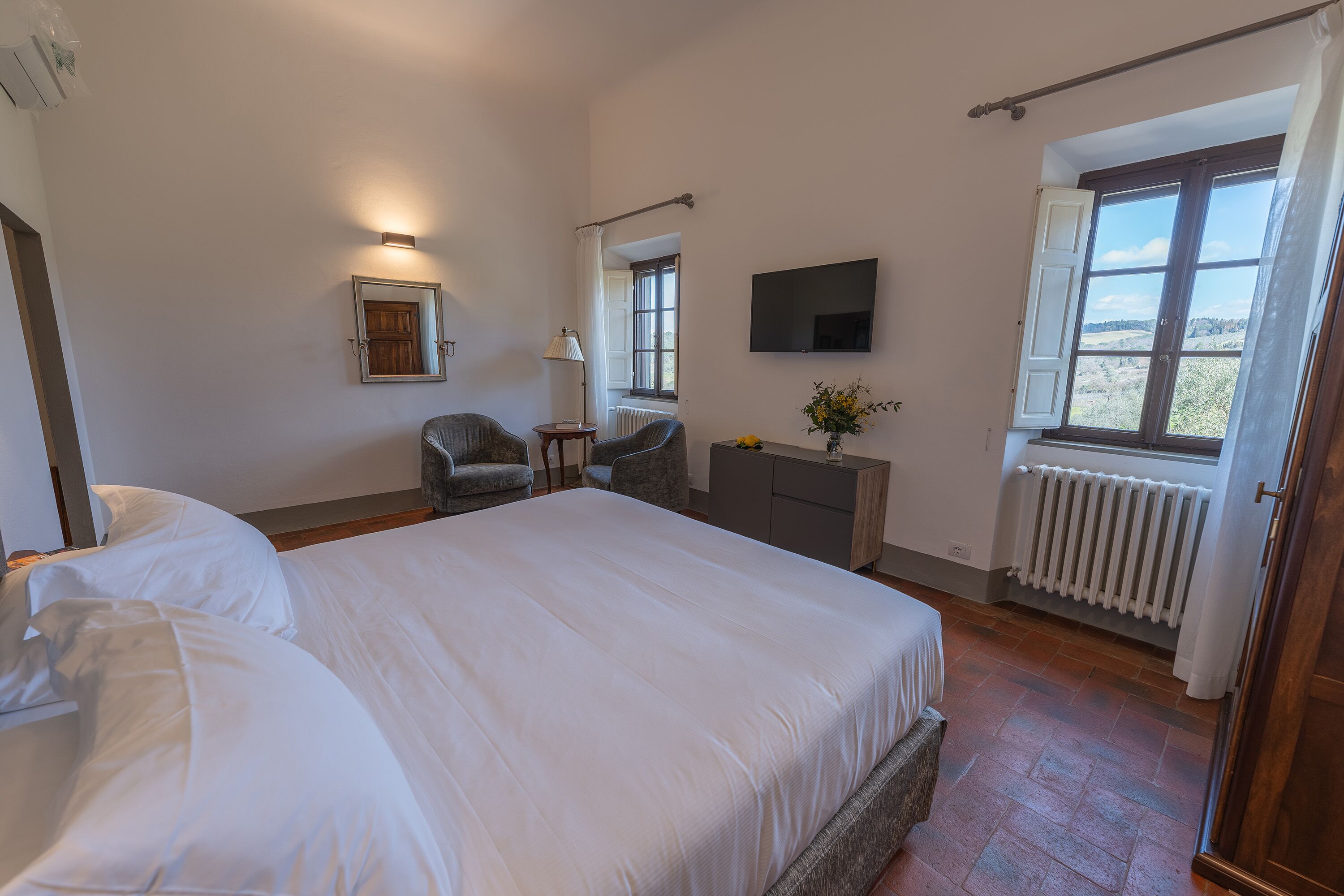 A bedroom with a large bed, a desk, a chair, a TV, and a window with curtains.