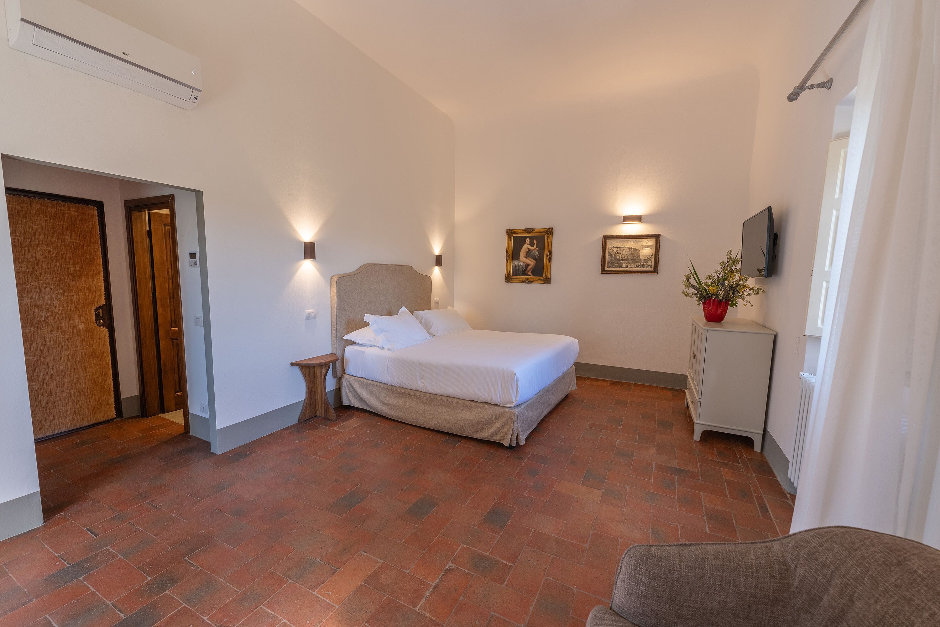 A bedroom with a bed, a nightstand, a wall-mounted TV, and a small cabinet.