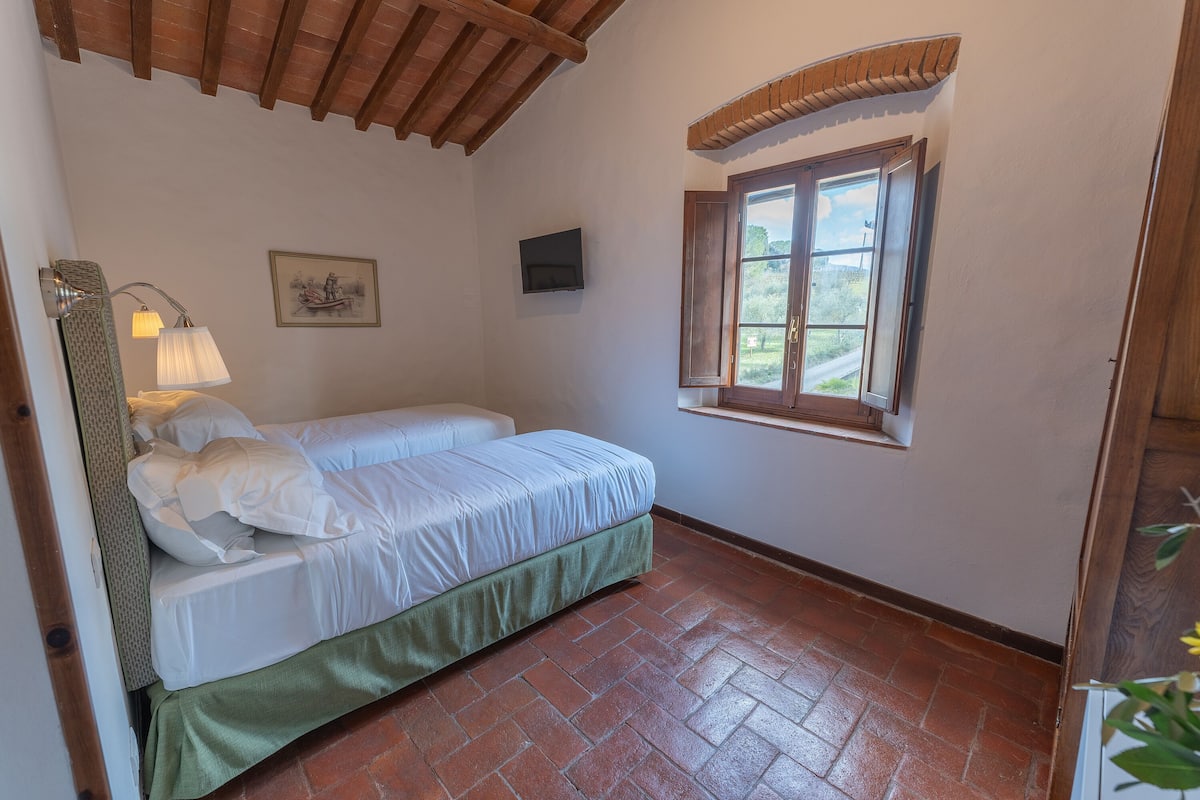 Un dormitorio con una cama, una ventana, un televisor y una lámpara.