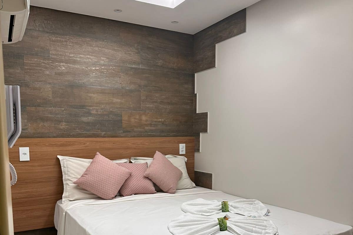 A modern bedroom with a wooden headboard, a bed with white linens, and a ceiling light fixture.