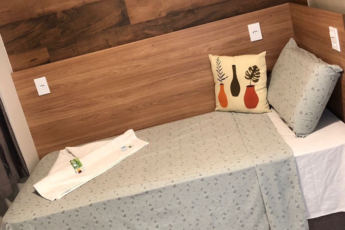 A small, cozy room with a wooden headboard, a single bed with a floral-patterned bedspread, and a pillow with a plant design.