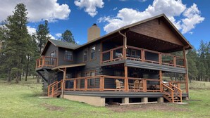 A two-story log cabin with a balcony and outdoor seating area. - Greer Pershing Cabin in the Meadow (Greer)
