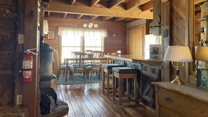A rustic cabin interior with a wooden dining area, a bar, and a fireplace. - Greer Pershing Cabin in the Meadow (Greer)
