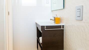 A modern bathroom with a white toilet, a wooden floor, a white sink with a dark cabinet, and a mirror on the wall.
