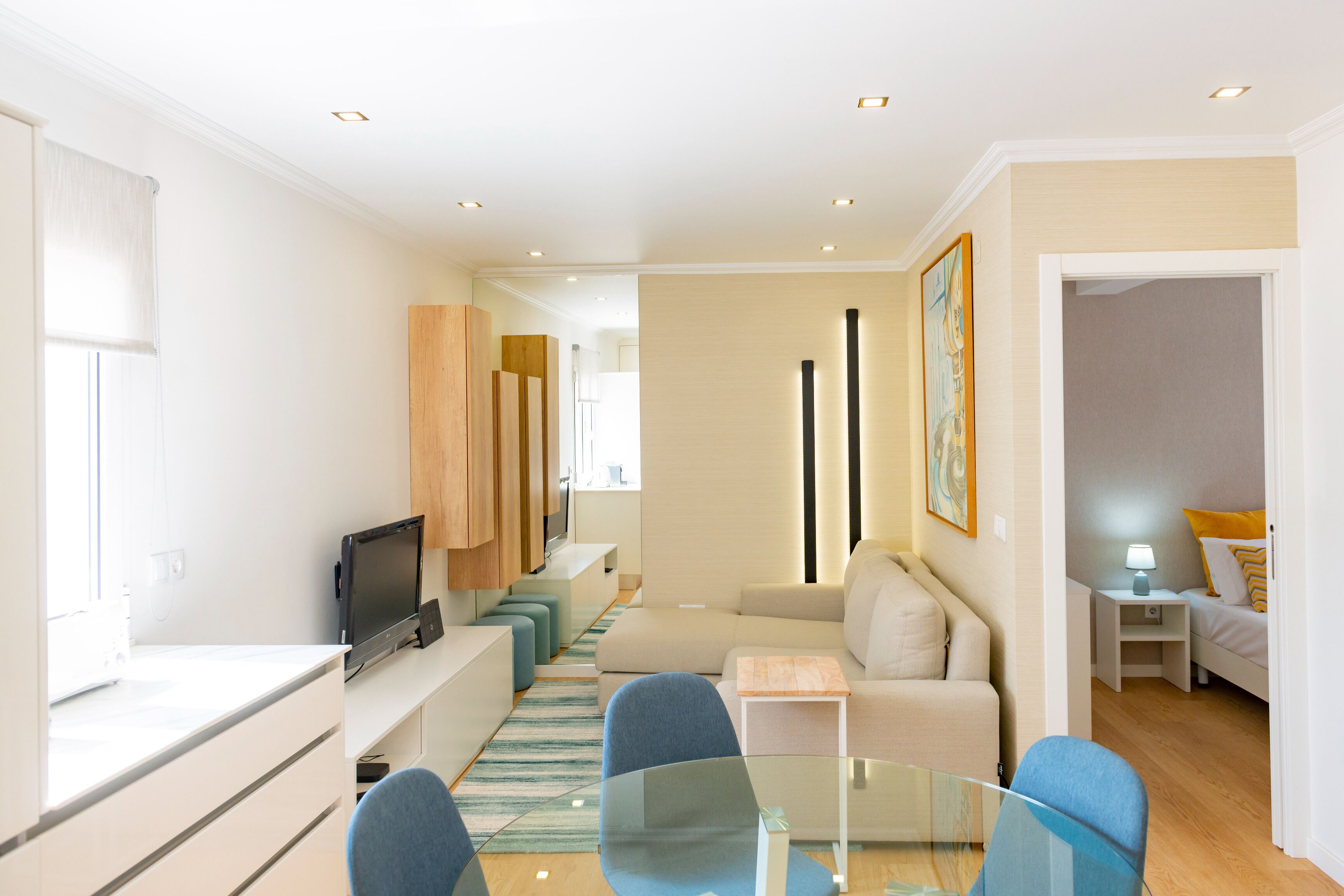 A modern living room with a glass coffee table, blue chairs, a beige sofa, and a flat-screen TV.