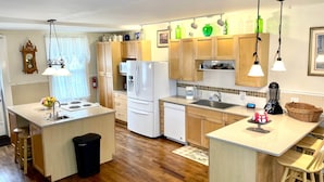 A modern kitchen with wooden cabinets, a central island, a refrigerator, a sink, and pendant lighting.